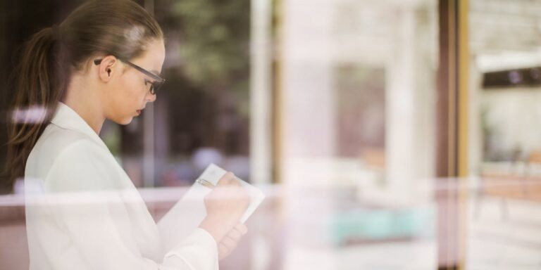 Zakelijke vrouw schrijft geconcentreerd iets op terwijl ze naar buiten kijkt, symbool voor reflectie bij ACT-therapie voor managers.